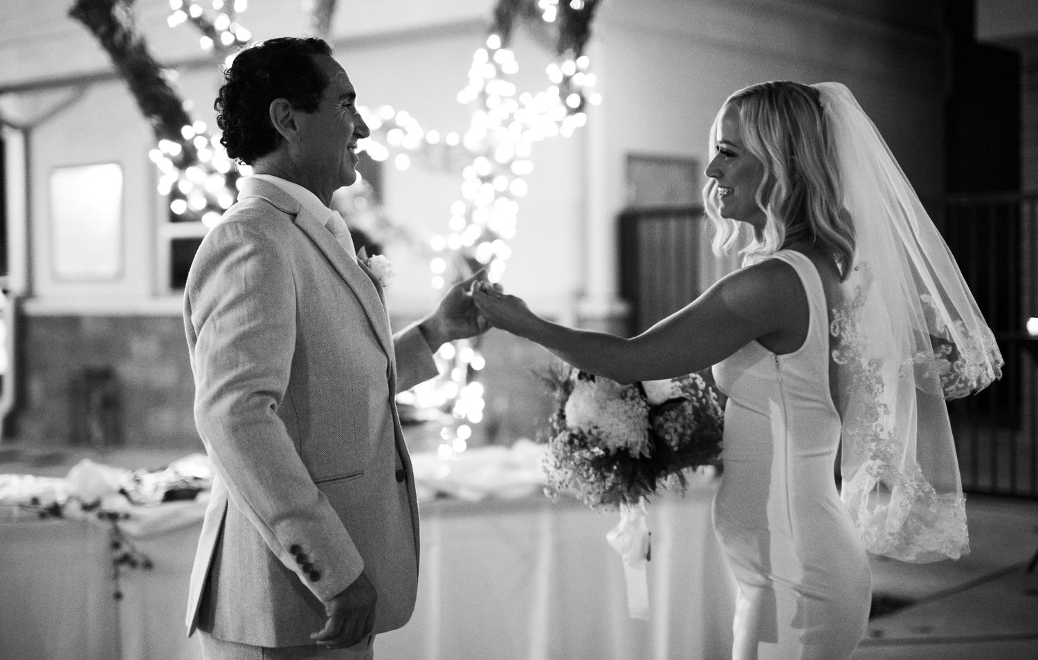 Black and white photo of a bride and groom holding hands and smiling during their wedding reception.