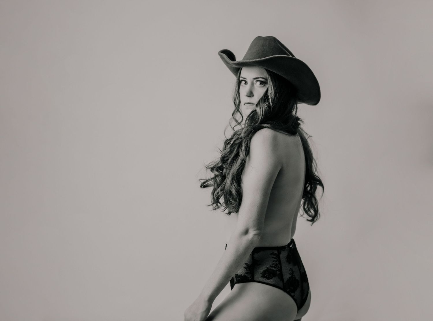 Black and white portrait of model in black shorts and cowboy hat posing against light background.