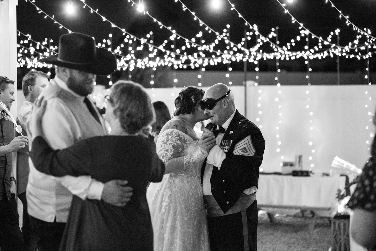Black and white wedding reception photo of bride and groom sharing a dance under twinkling fairy lights.
