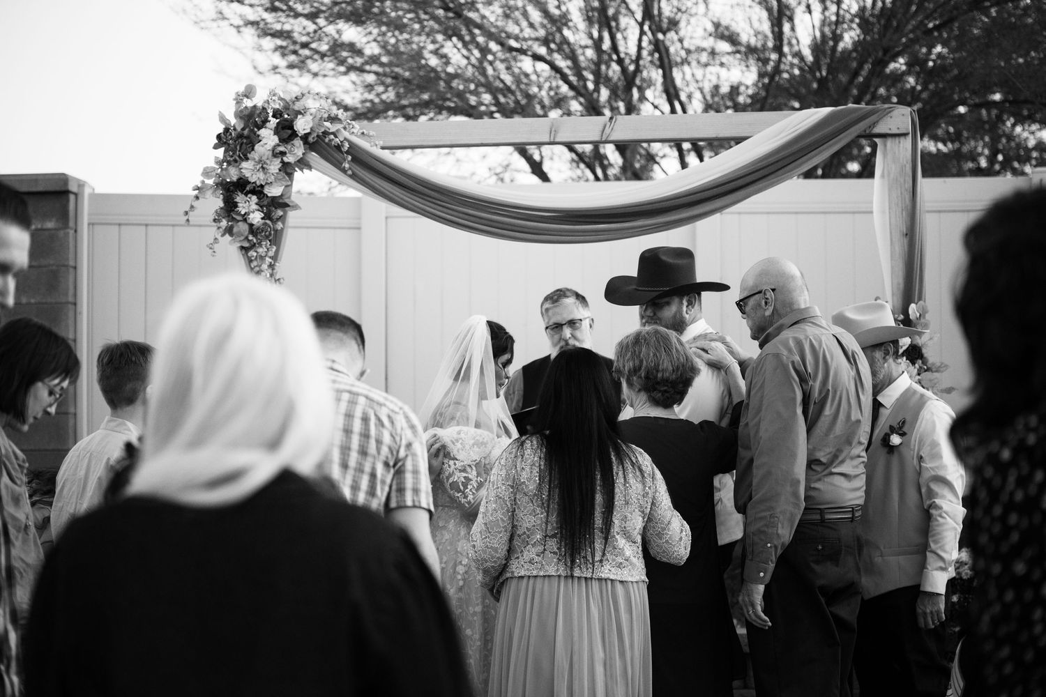 Black and white photo of a wedding ceremony outdoors with guests gathered around the couple at the altar.