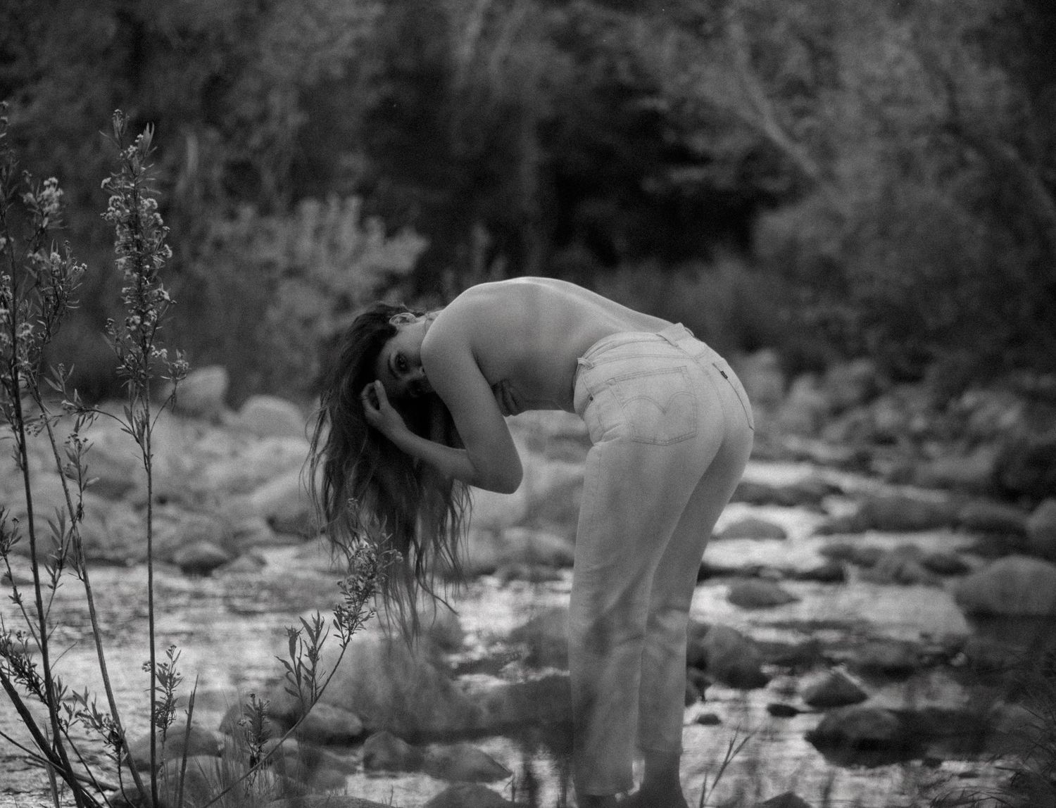 Artistic black and white photograph of figure bending over by rocky stream.