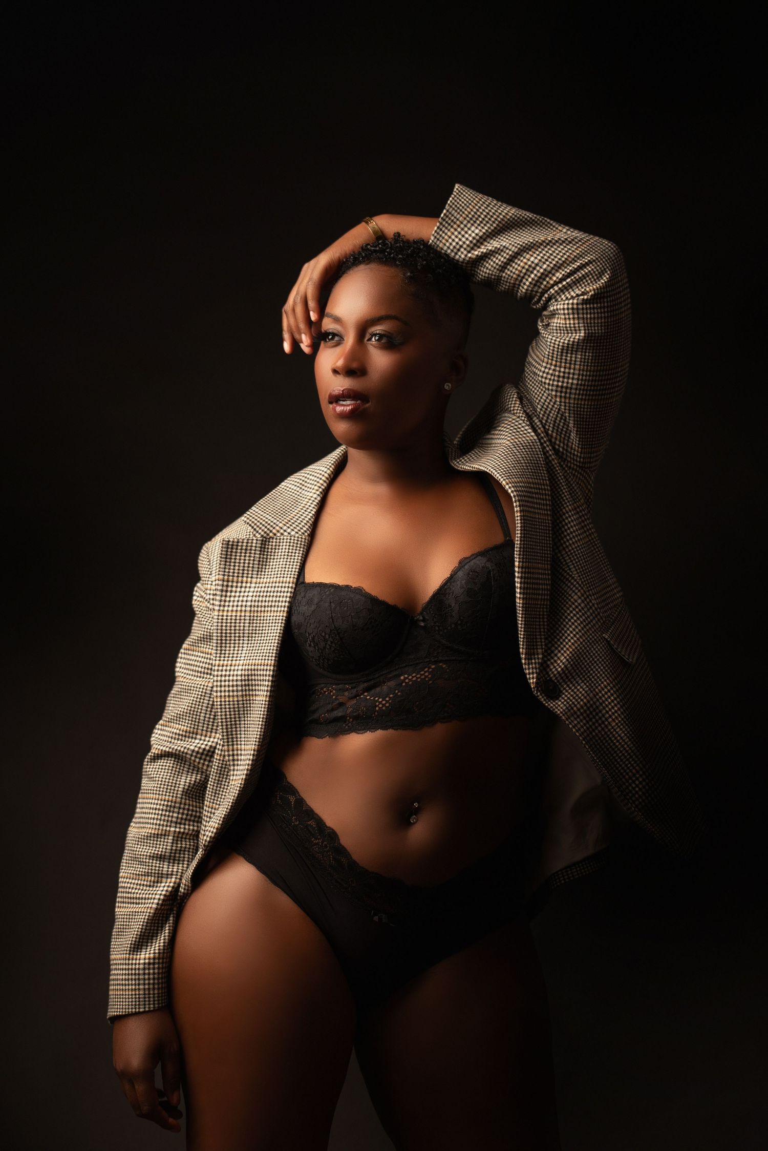 Studio portrait featuring black lingerie and an oversized plaid blazer in dramatic lighting against dark background.