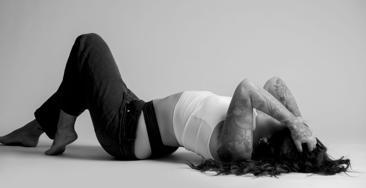 Artistic black and white photograph showing a person lying on the floor in a relaxed pose wearing a tank top and jeans.