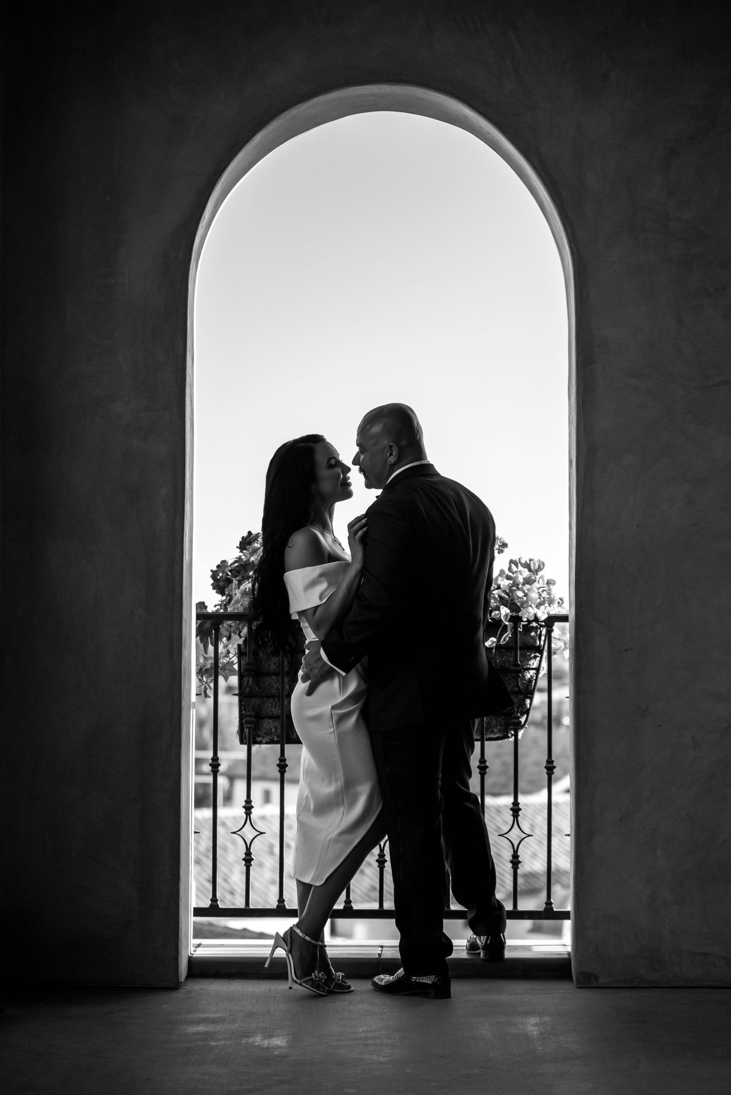 A romantic silhouette of a couple embracing in an arched doorway, captured in black and white photography.