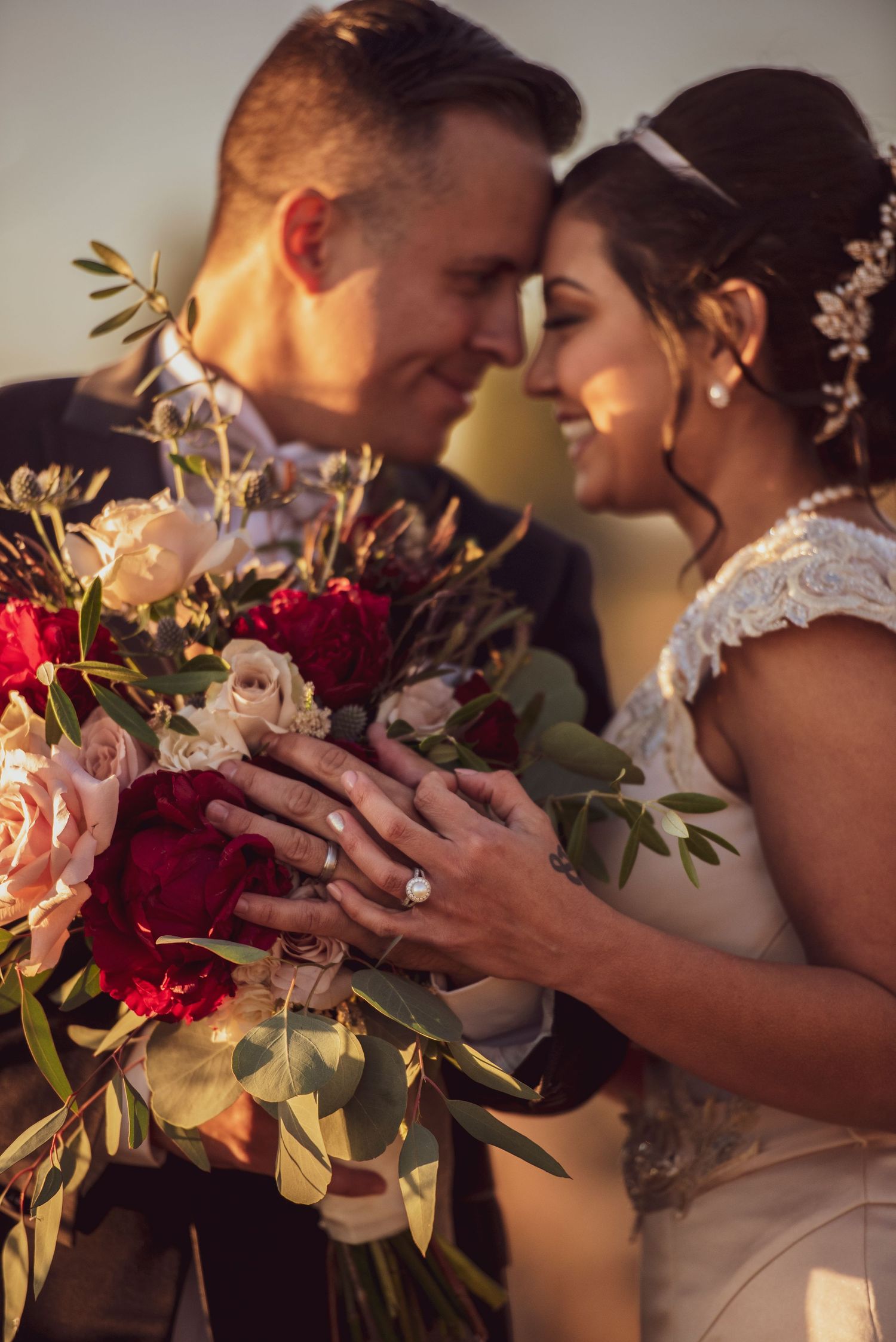 A romantic wedding moment between newlyweds sharing an intimate close-up with a beautiful red and pink floral bouquet.