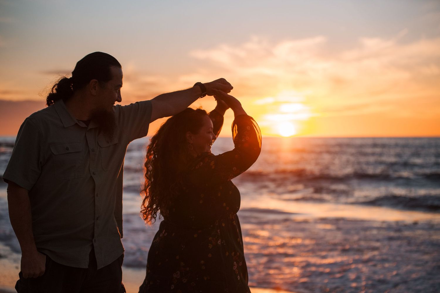 Couple dancing romantically on a beach at sunset with golden ocean waves in the background.