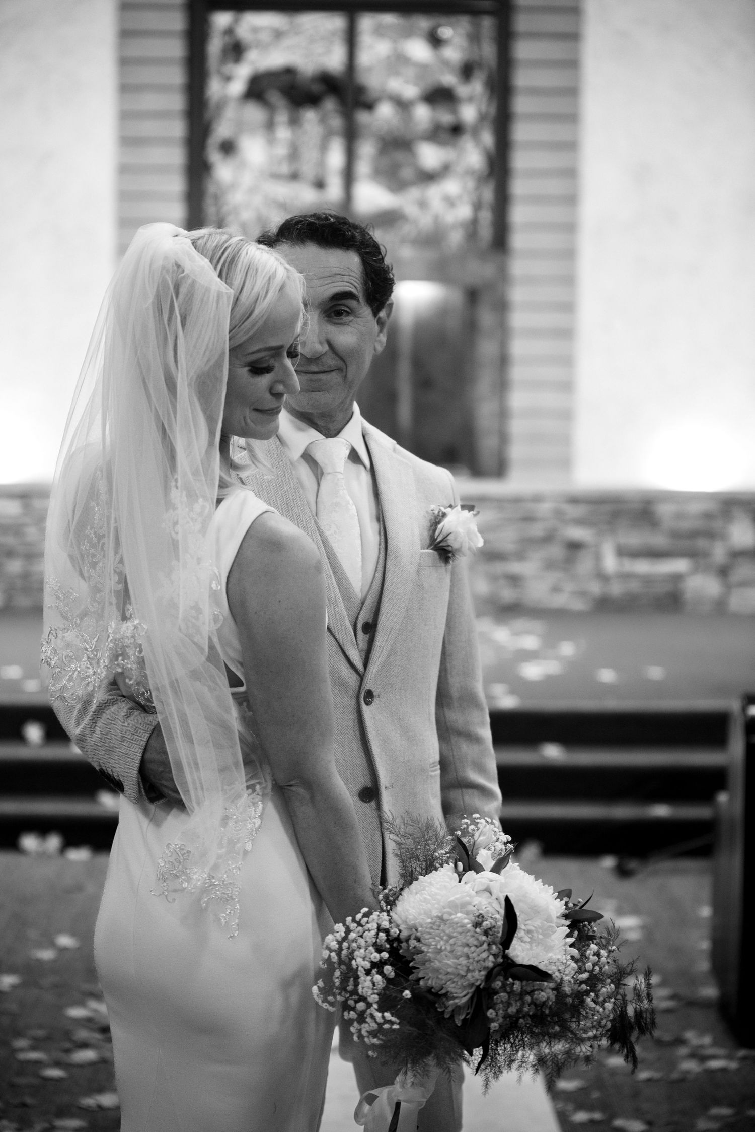 Black and white photo of a bride and groom sharing a tender moment in a church aisle, bride holding a bouquet.