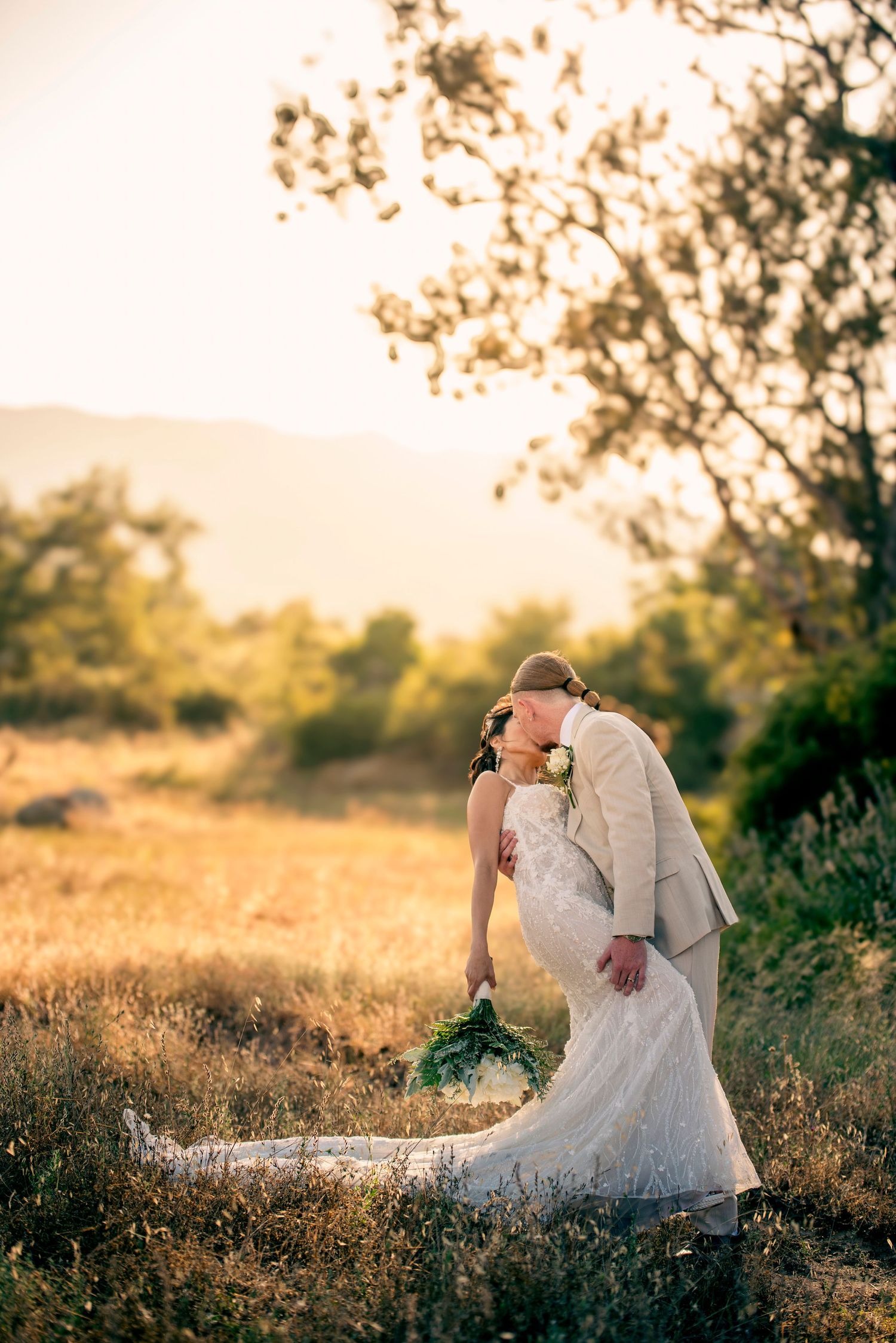 Romantic sunset wedding portrait in a golden field with soft ethereal lighting and natural backdrop.