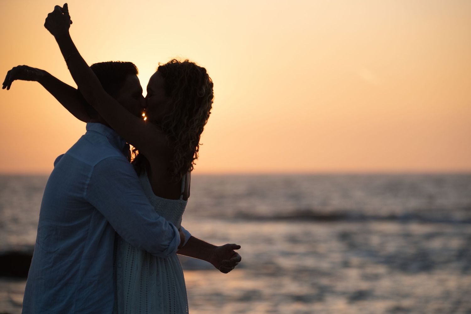 A couple embraces in silhouette against a golden sunset over the ocean.