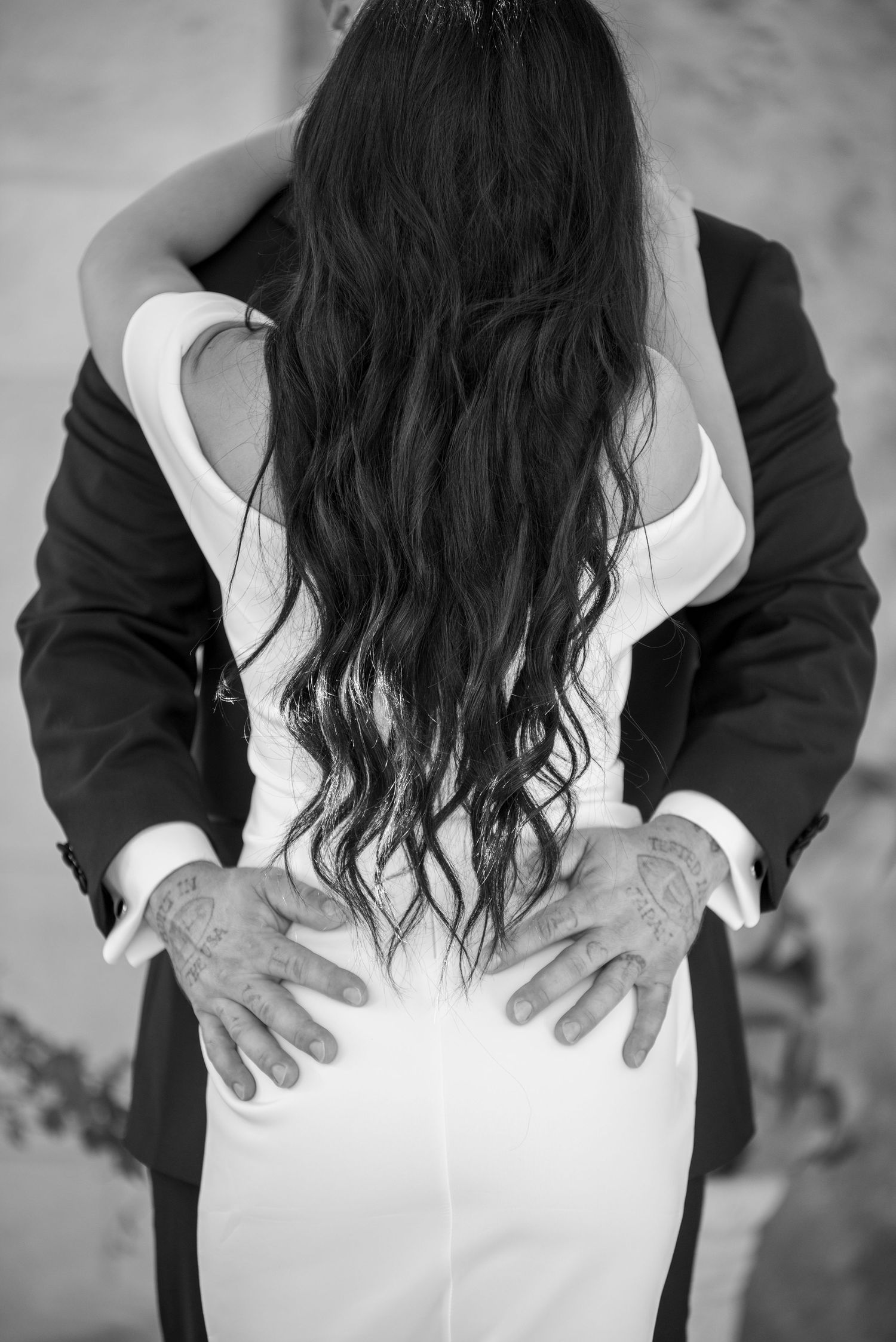 Black and white romantic photo showing two people embracing, with long dark wavy hair cascading down a white dress.