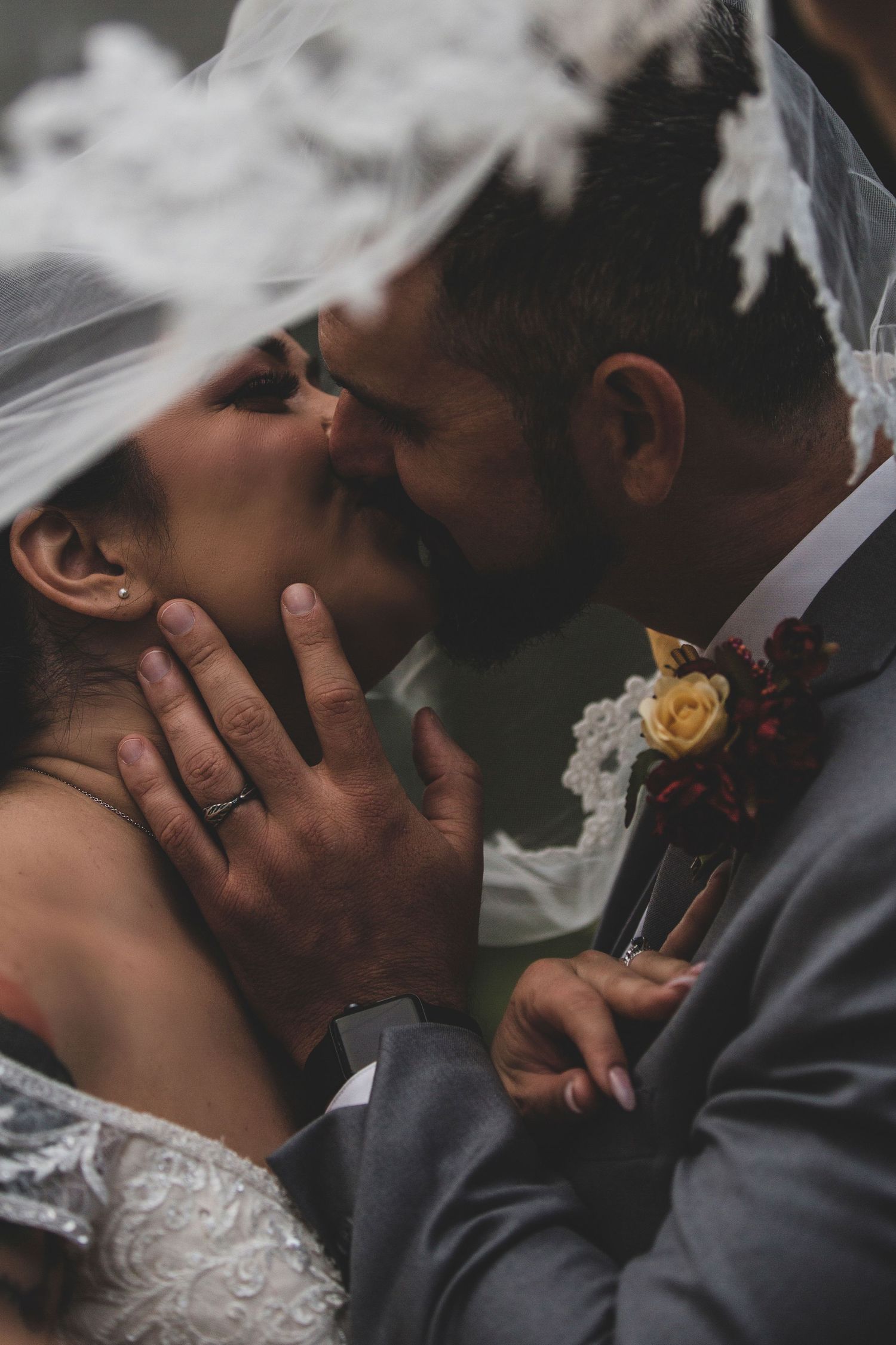 A romantic wedding moment captured through a delicate veil with a yellow boutonniere on the groom's lapel.