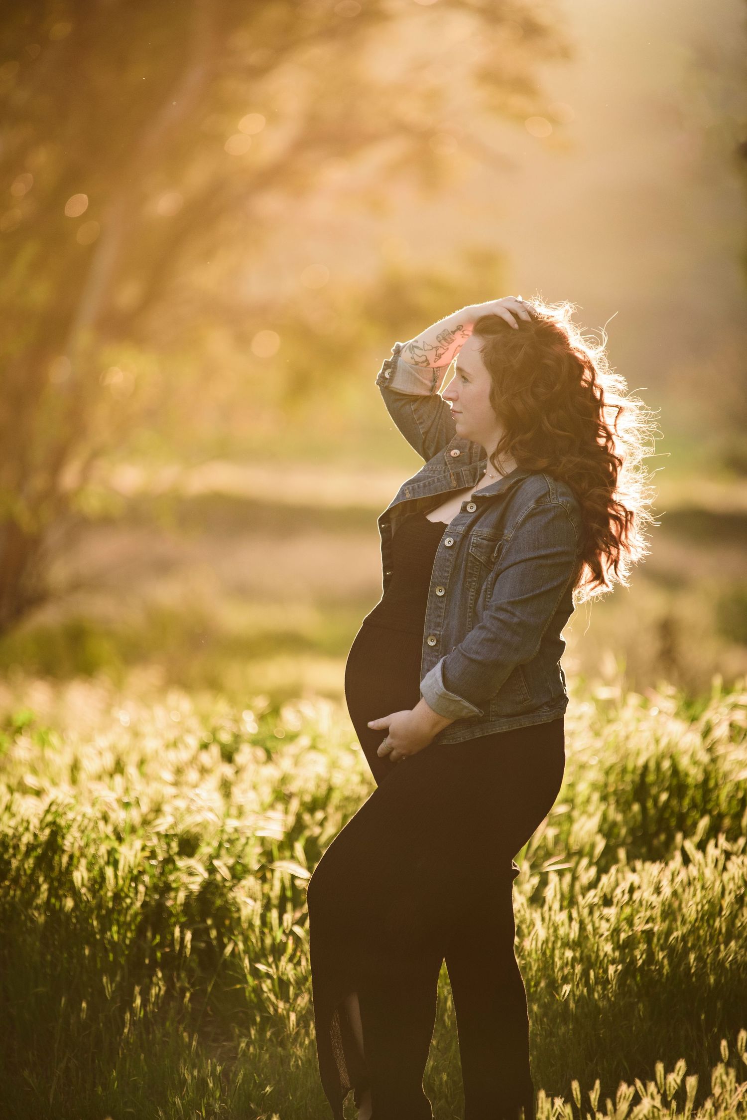 Silhouetted maternity portrait in denim jacket against golden sunset light.