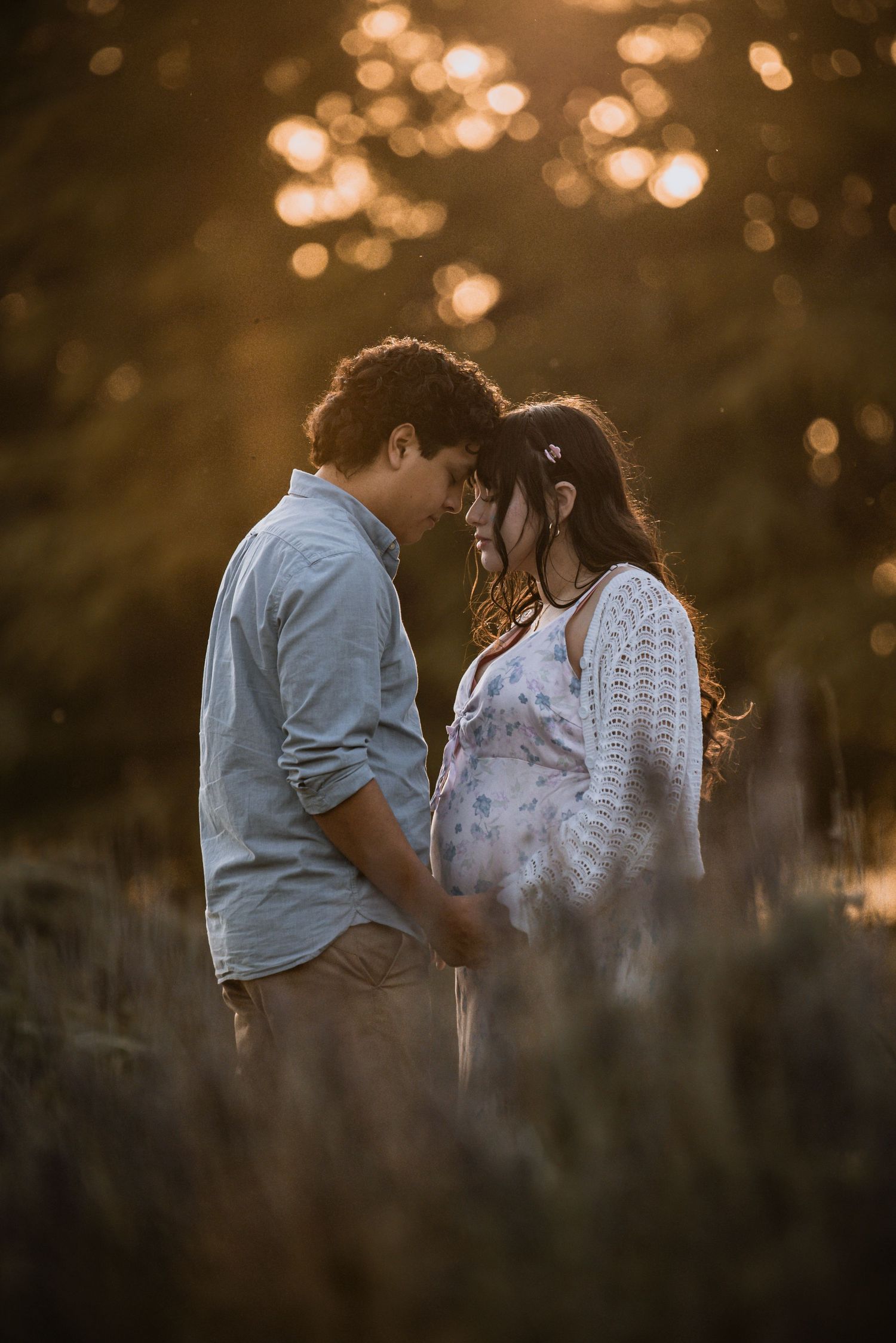 A romantic couple shares an intimate moment at sunset with bokeh lights glowing in the background.
