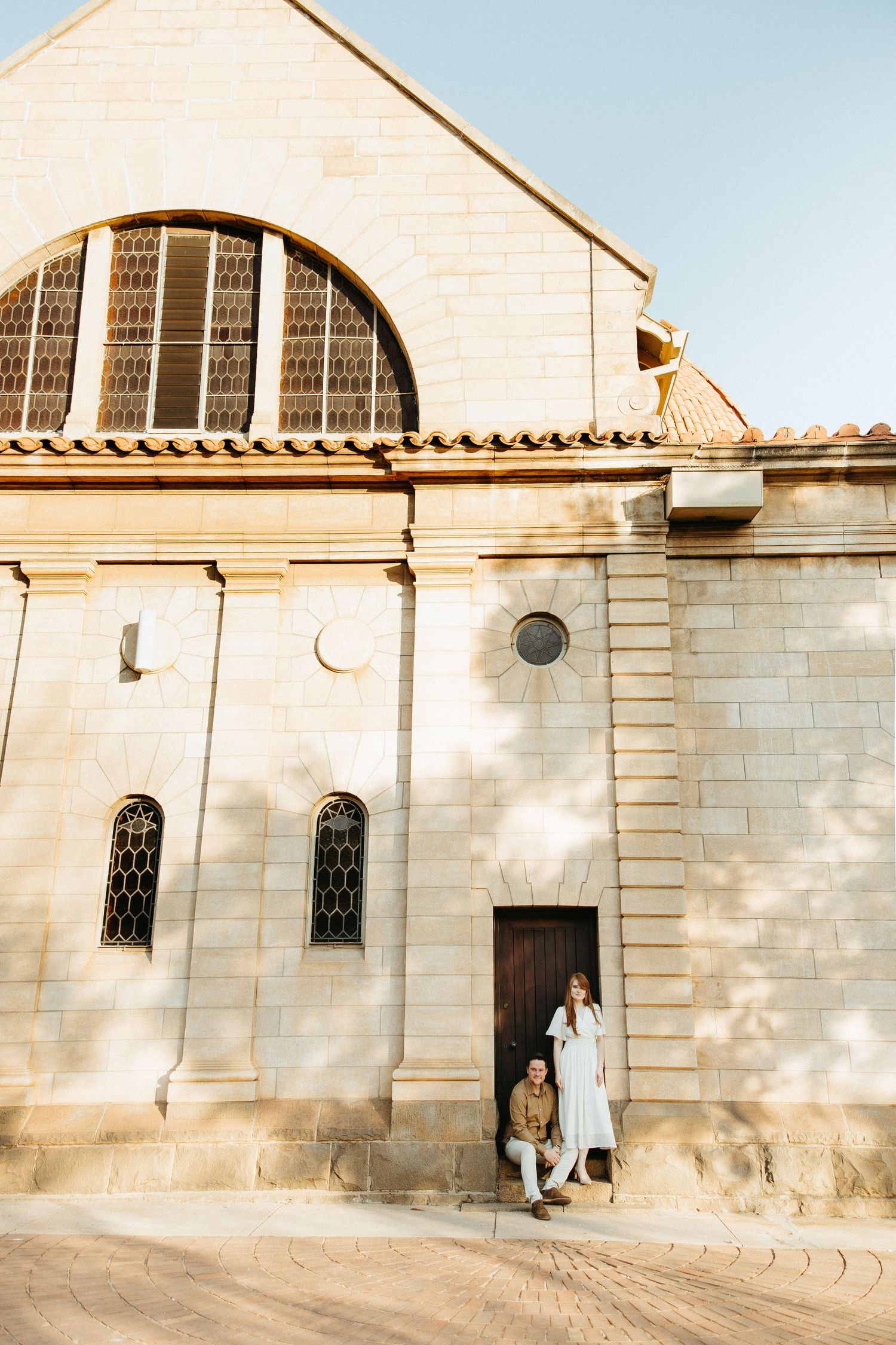 Engaged Couple standing on a step in front of a wooden door fitted into old sandstone church.