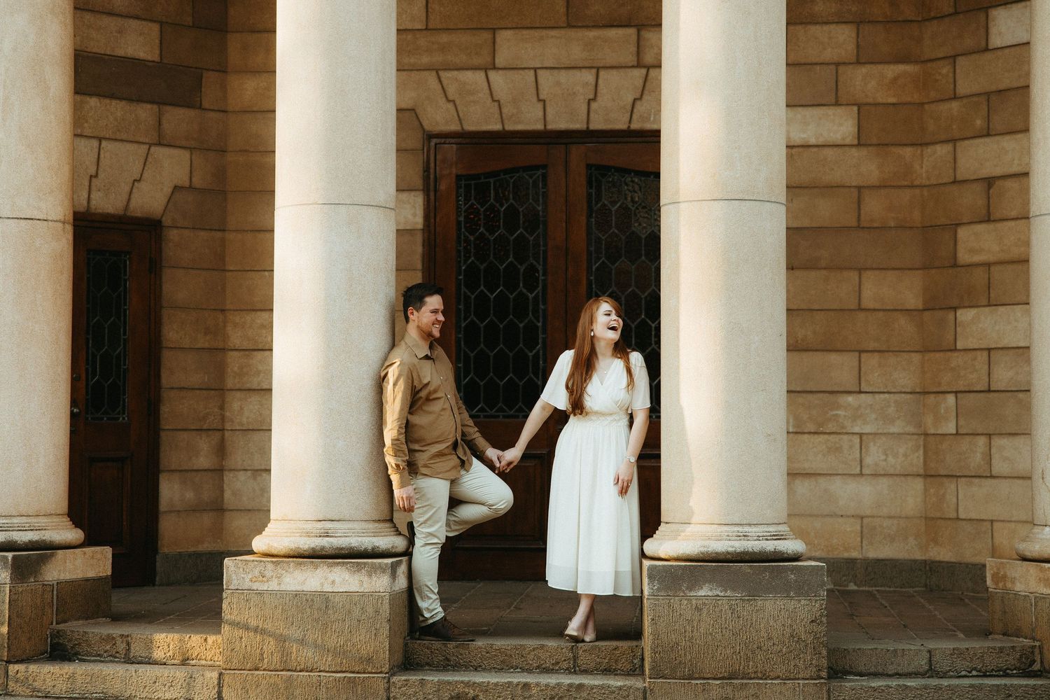 Engaged Couple standing between two sandstone pillars, laughing.