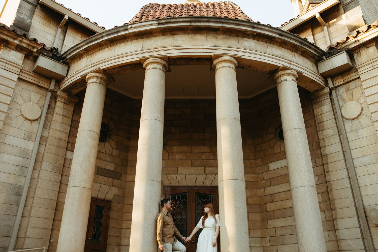 Engaged Couple standing between two sandstone pillars, surrounded by the old sandstone church