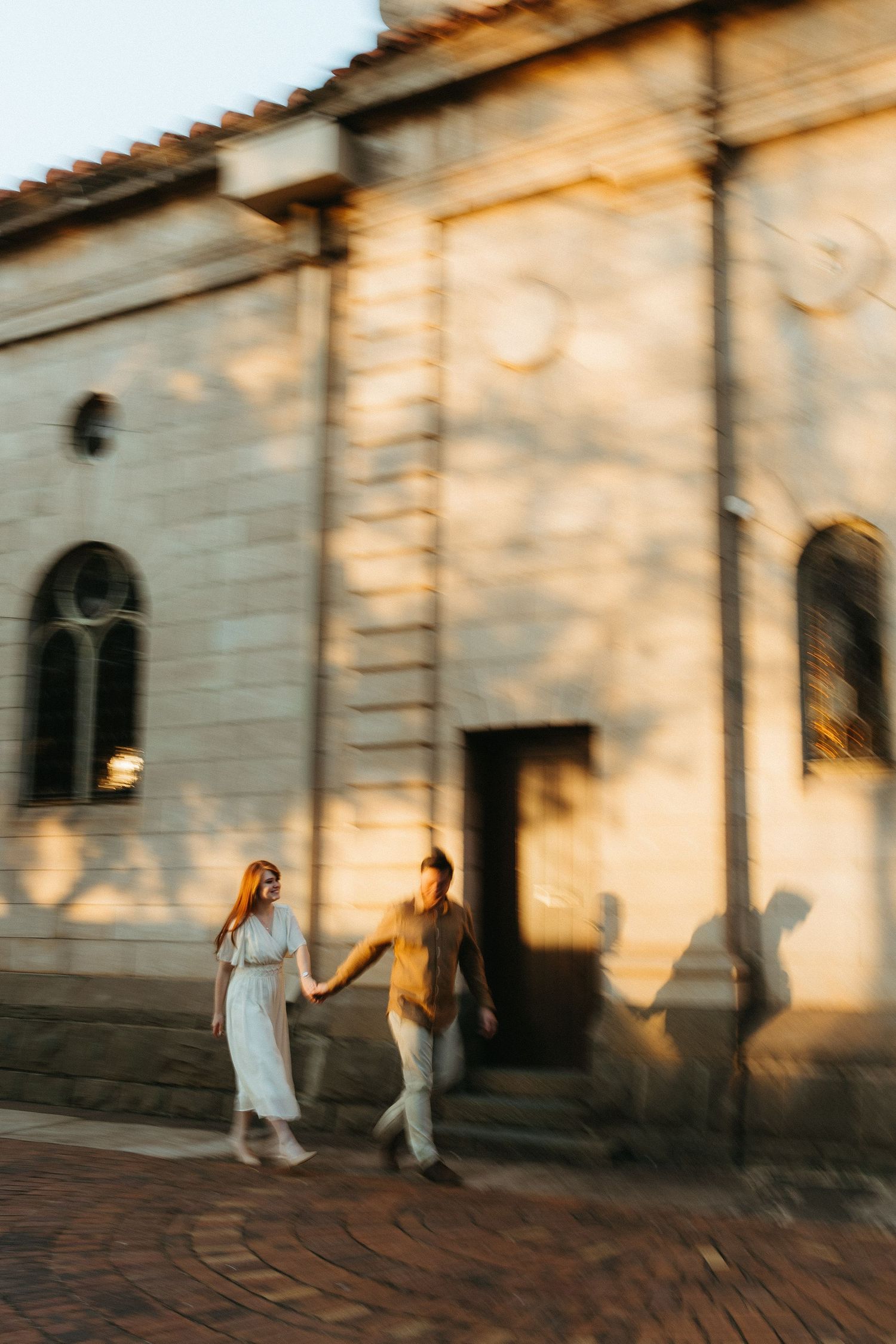 Blurry photo capturing the motion of a couple holding hands and walking in front of an old sandstone church