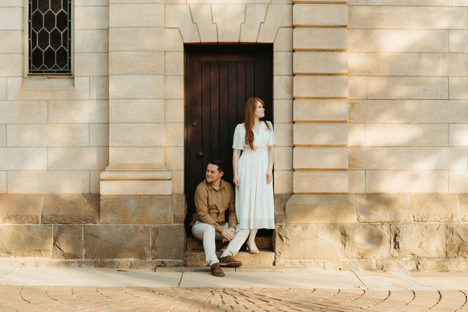 Engaged Couple standing on a step in front of a wooden door fitted into old sandstone church.