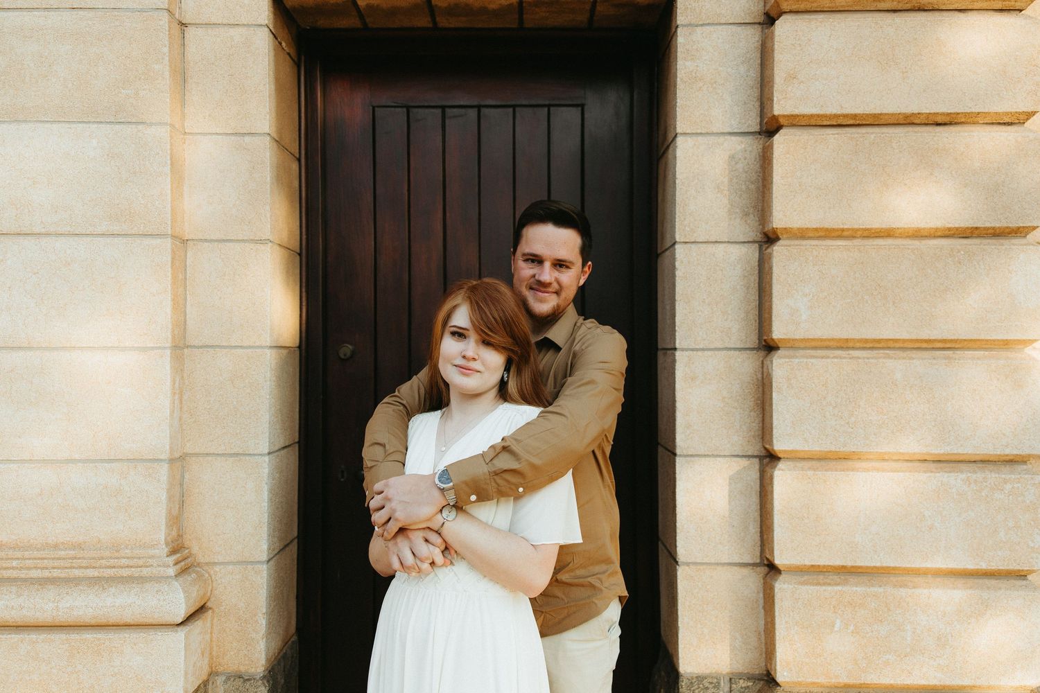 Engaged Couple standing in front of a wooden door fitted into old sandstone church building.