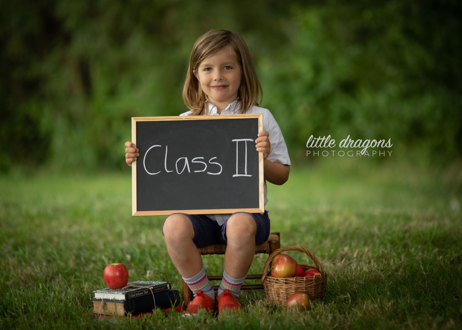 Back to school themed photo shoot in a lush green garden setting with chalkboard and red apples.
