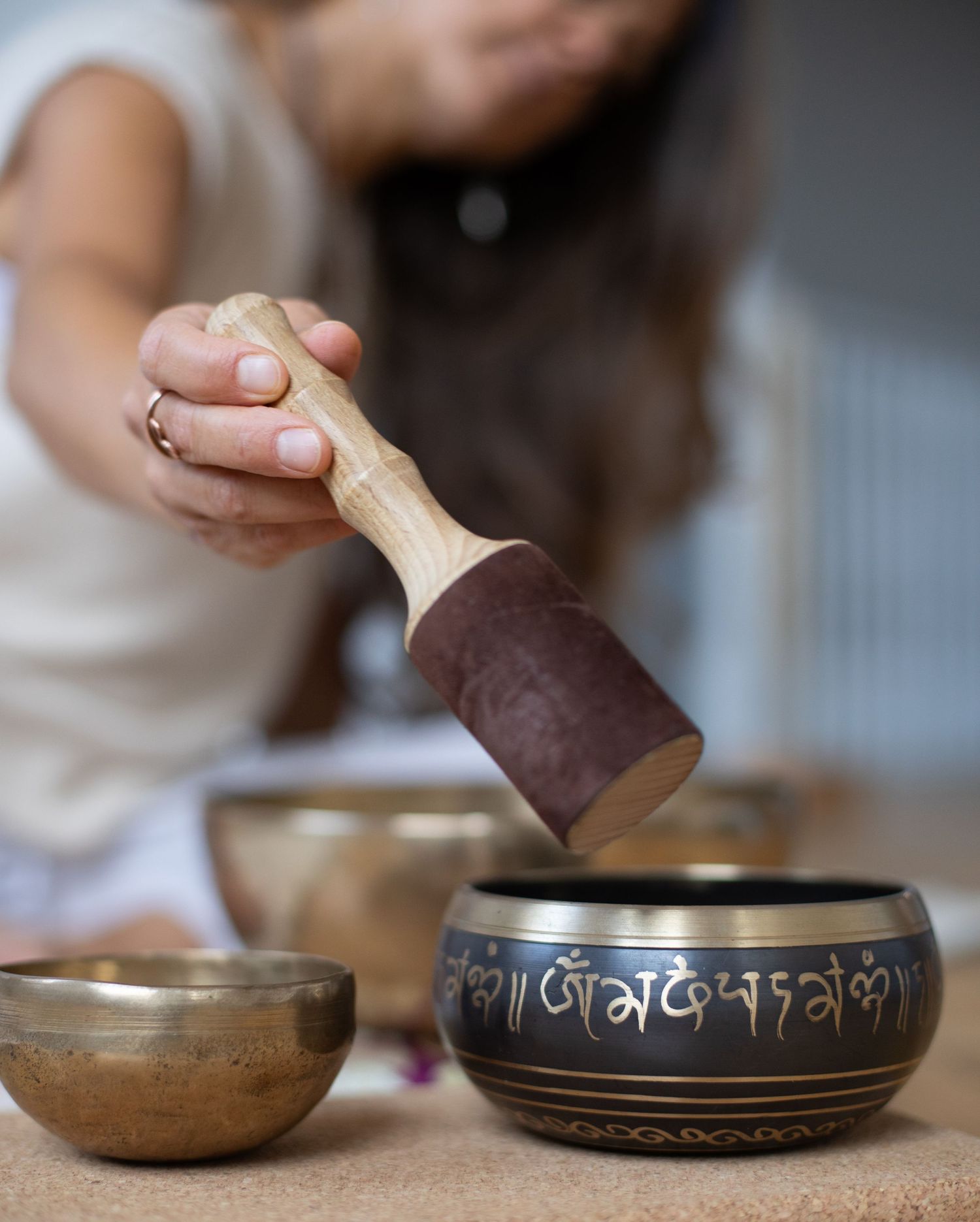 Close-up sequence showing hands striking a Tibetan singing bowl with a wooden mallet in a meditative setting.