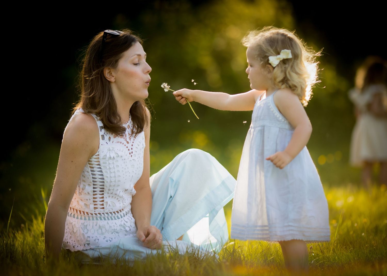 Children in white dresses play together in a sunlit grassy field during golden hour.