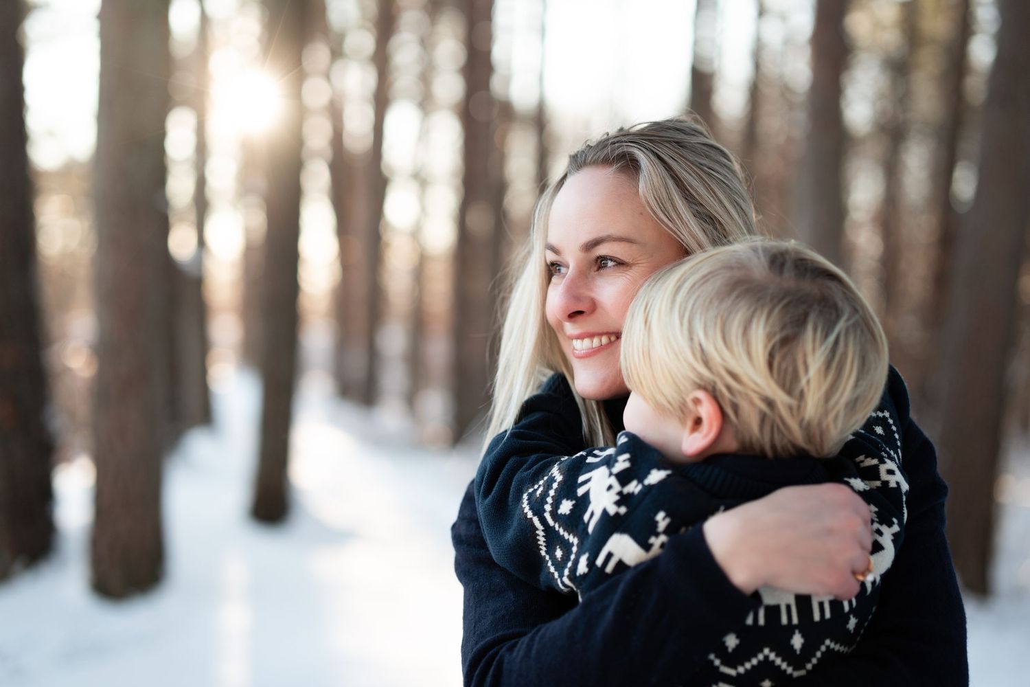 Fotografering av mor og sønn som står ute i snøen i varme gensere. Mor bærer på sønnen sin.