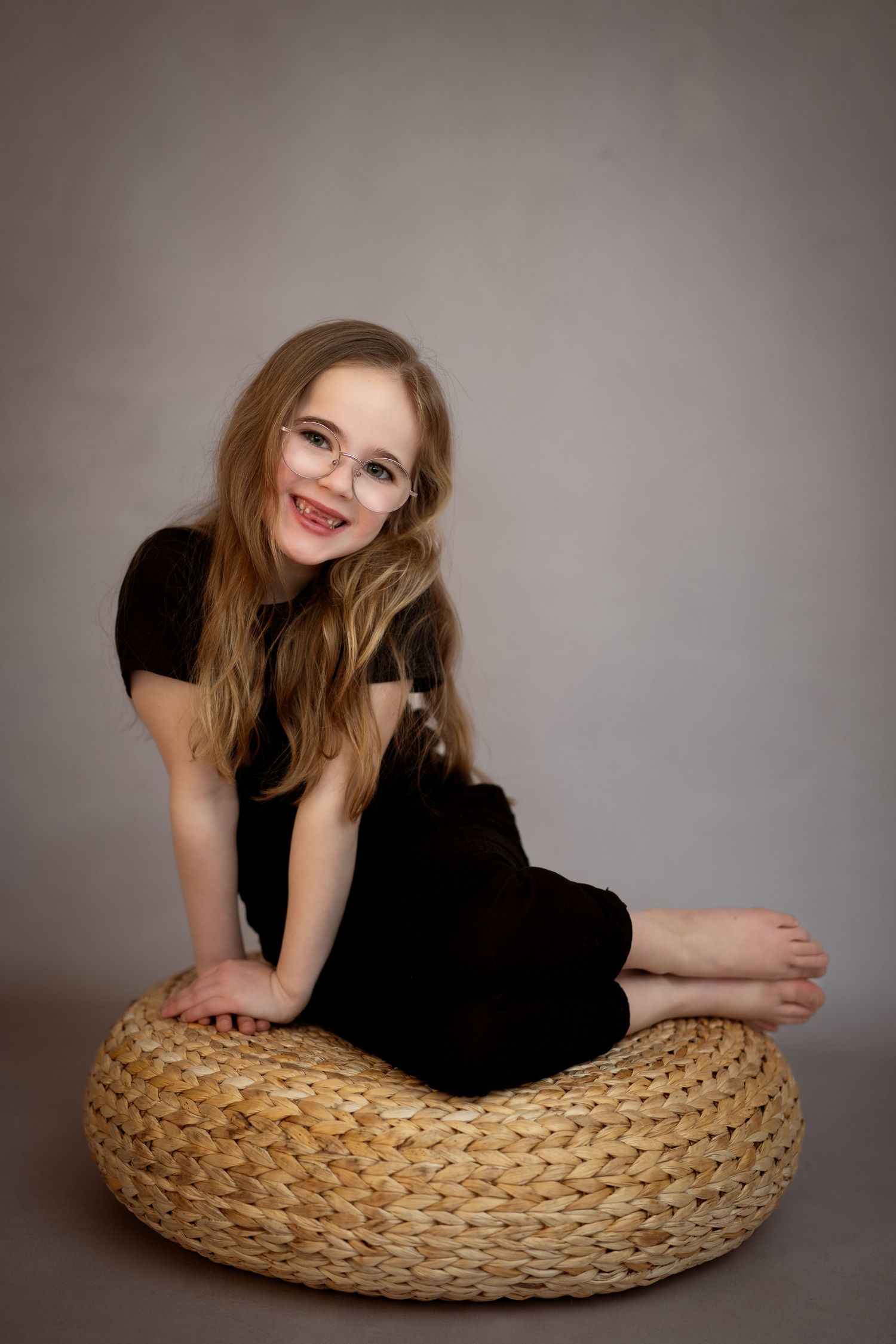 Portrettfotografering av ei jente på 5 år, iført i mørke klær, i et studio med grå bakgrunn. Jenten smiler.