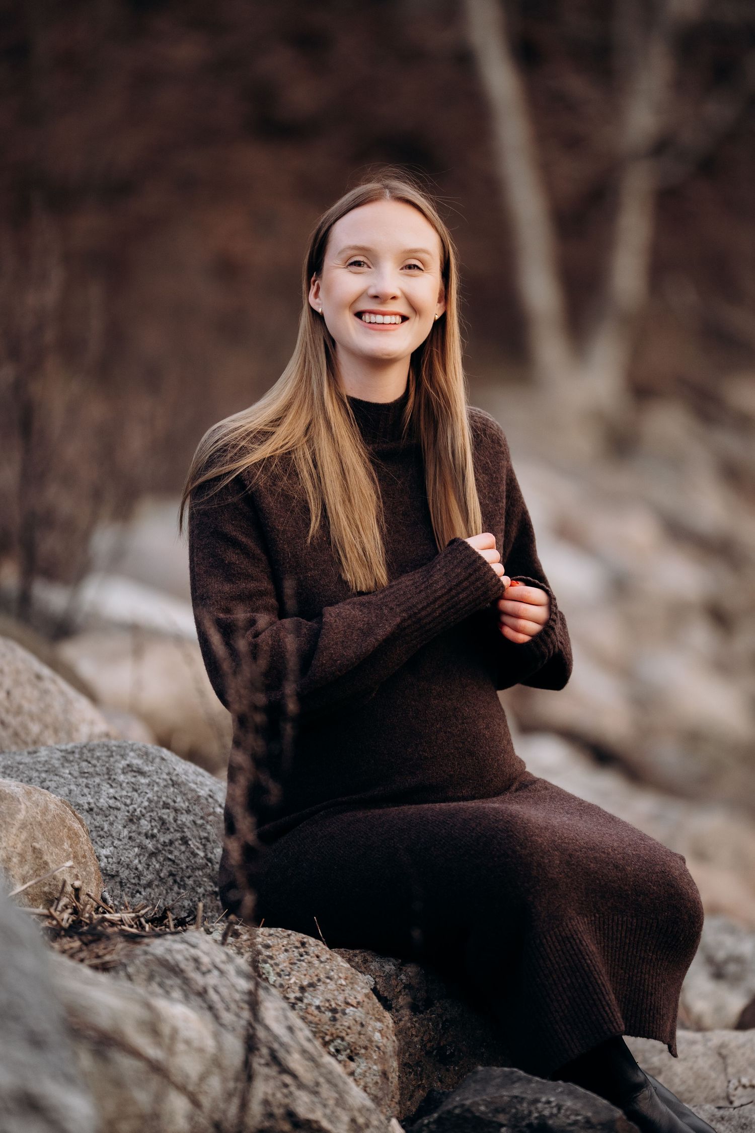 Portrett fotografering av gravid dame - sitter på en stein og smiler mot kamera.