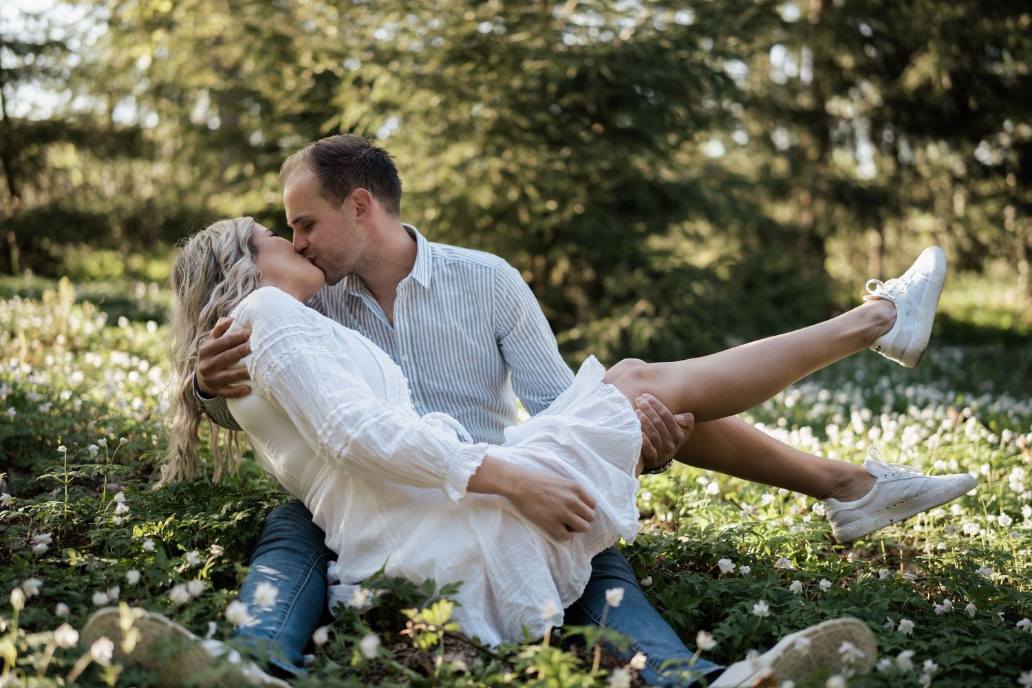 Parfotografering av et par i lyse antrekk som kysser i en hvitveis eng.