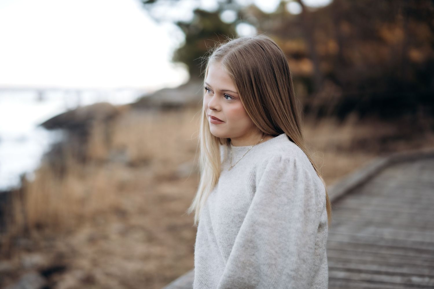 Konfirmantfotografering - Tenåringsjente med lyst hår som sitter langs en bryggekant og kikker utover havet.