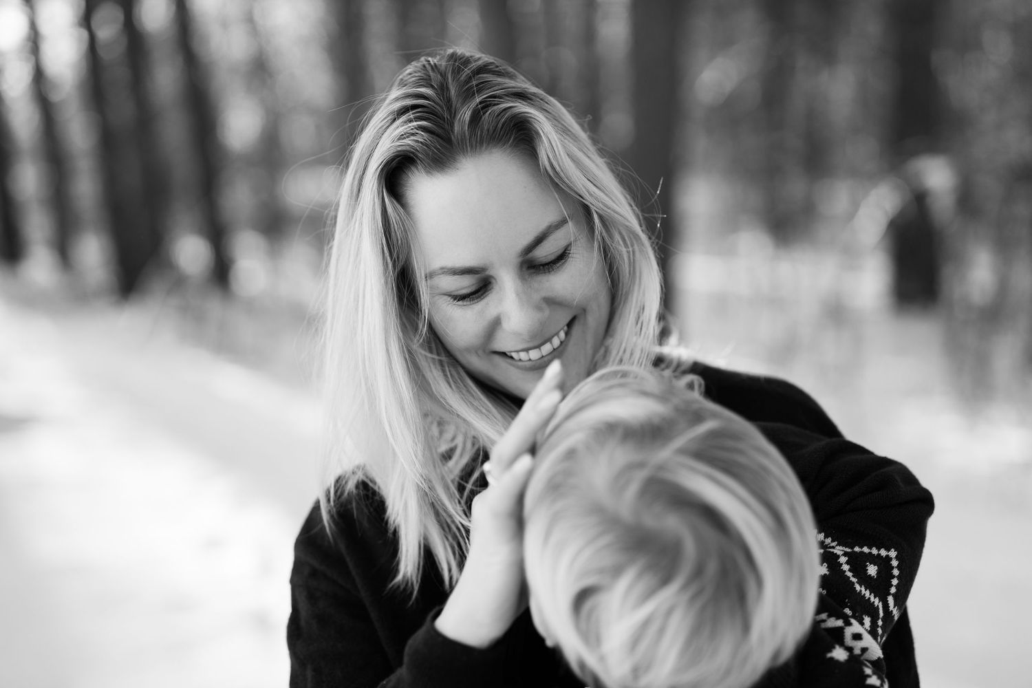 Familiefotografi av en mor som smiler mot sønnen sin. Moren er blond, og man ser kun bakhodet til sønnen.