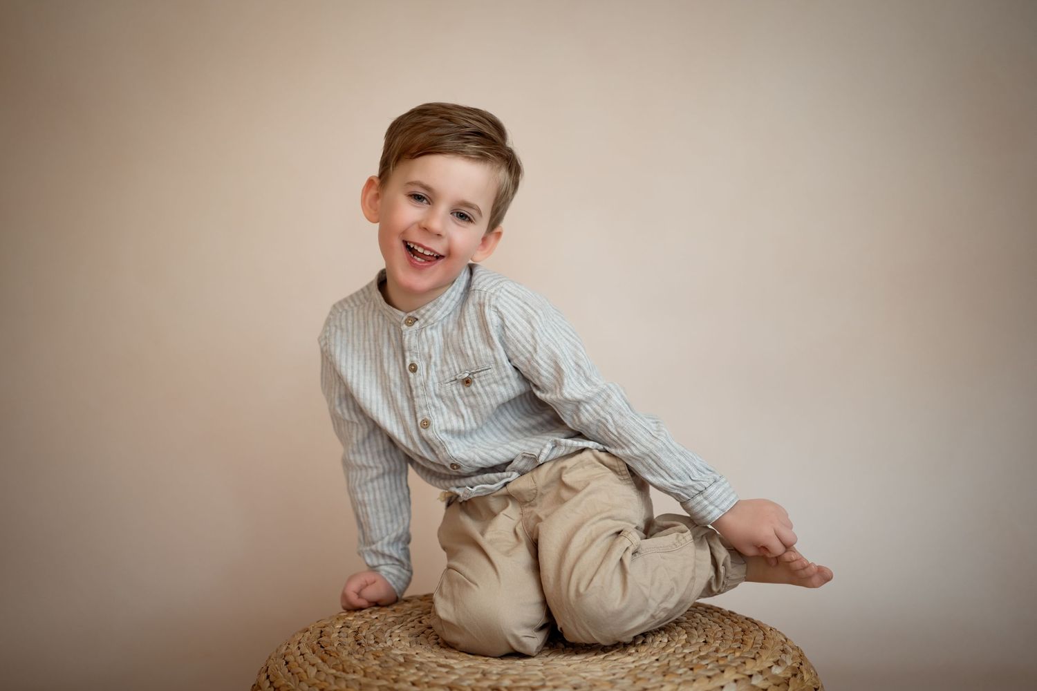 Portrettfotografering av en liten gutt som sitter i blå¨skjorte med en begie bakgrunn.
