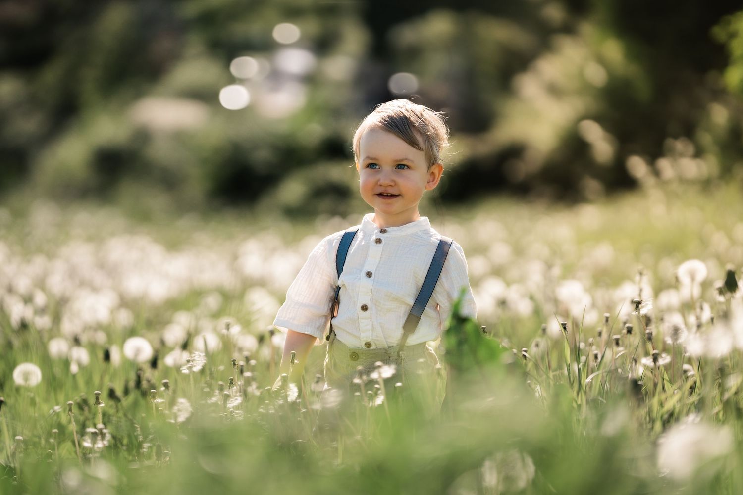 Barnefotografering av et barn som leker på en solfylt eng fylt med hvite villblomster på en lys sommerdag.