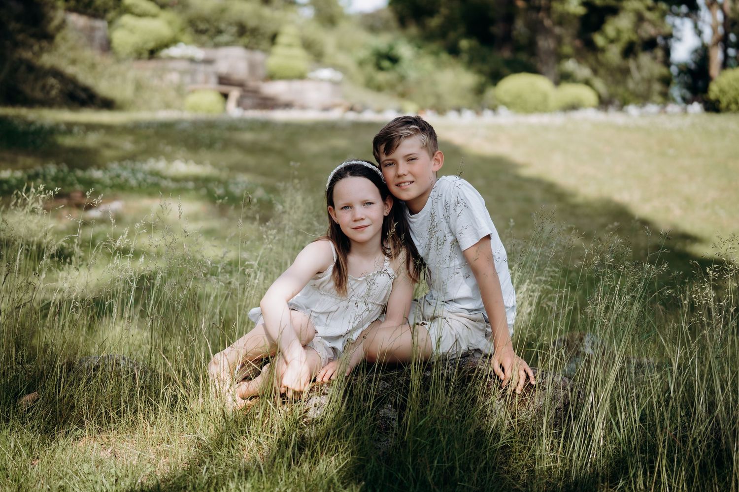 Naturlig søskenfotografering utendørs i Sandefjord – barn i sommerlys omgitt av gress og natur.