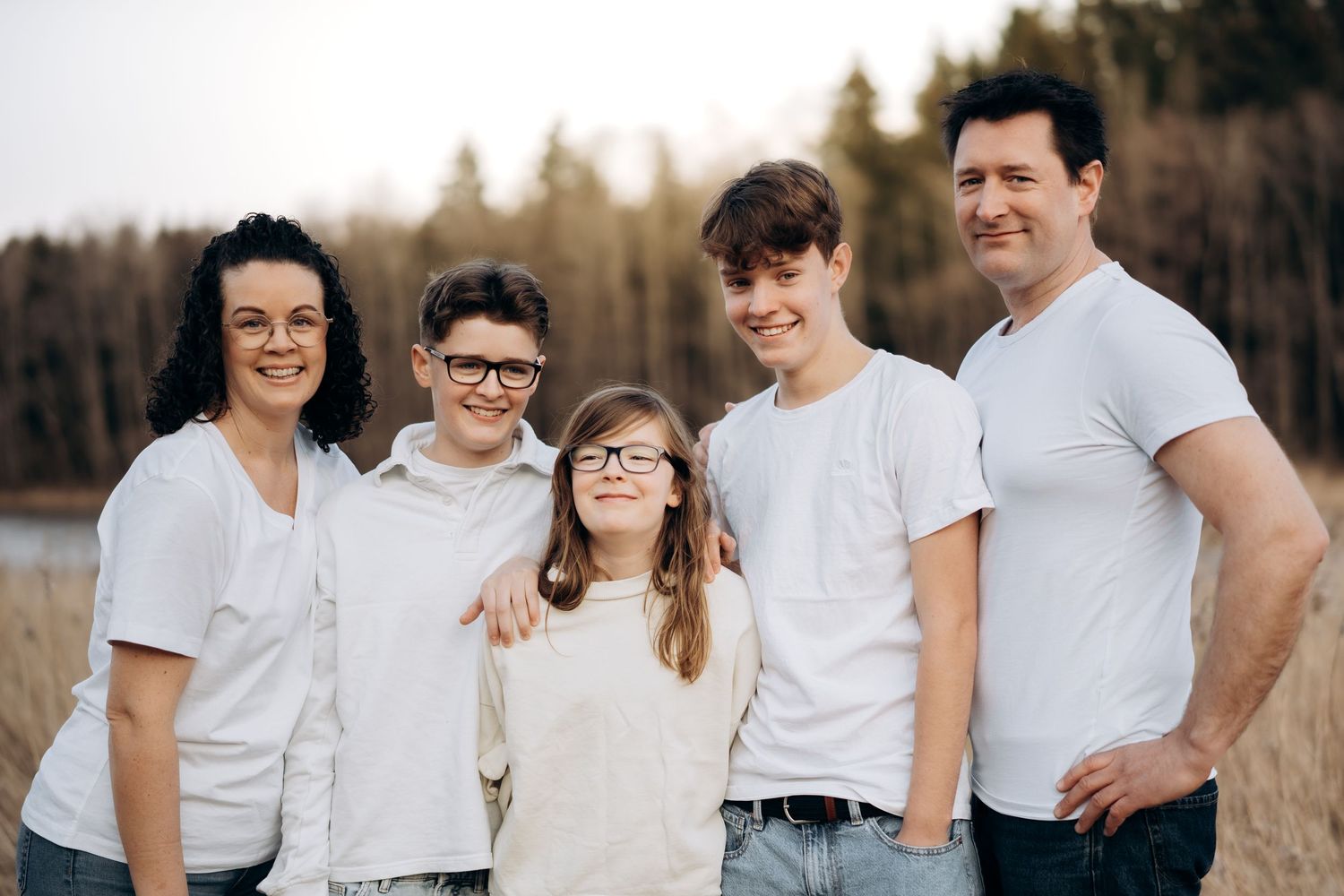 Familiefoto av to foreldre og tenåringsbarn i hvite overdeler, foran en åker.