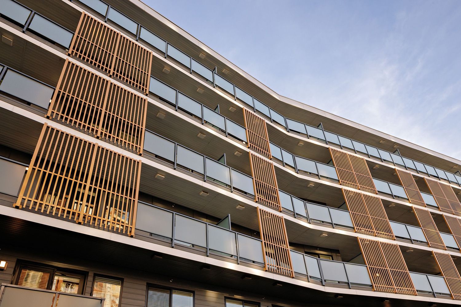 Modern apartment building exterior with wooden slat details and glass balconies against blue sky.