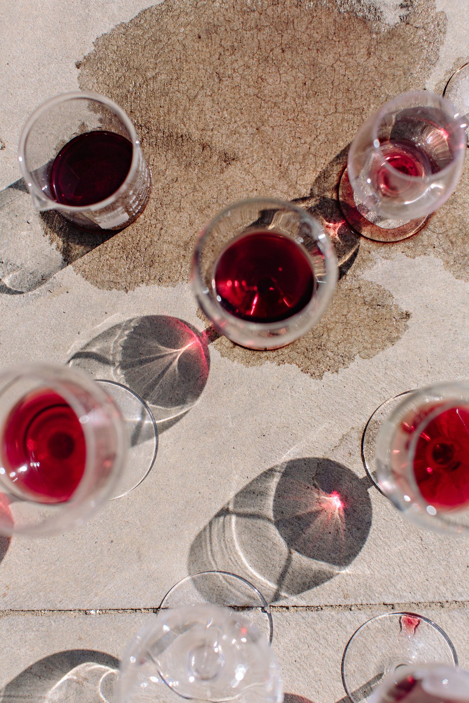 Overhead view of red wine glasses casting dramatic shadows on light colored stone or concrete surface.
