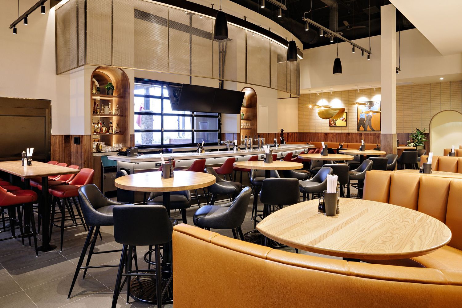 Modern restaurant interior with leather banquettes, round tables, and warm lighting under arched windows.