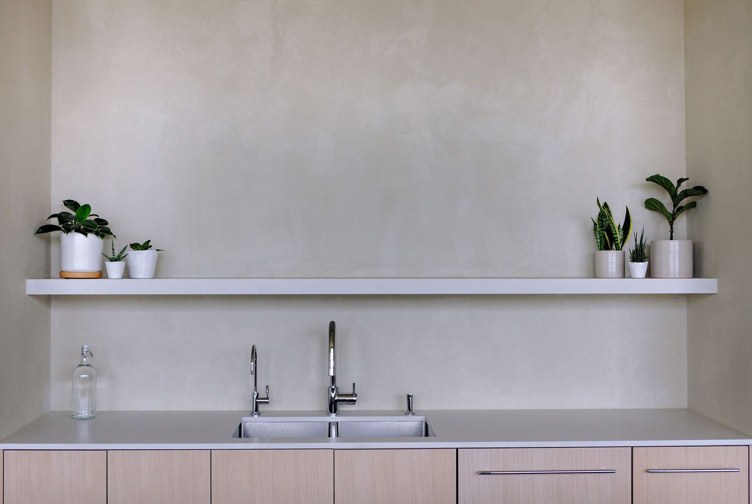 Modern minimalist kitchen design with white shelf displaying small potted plants above stainless steel sink.