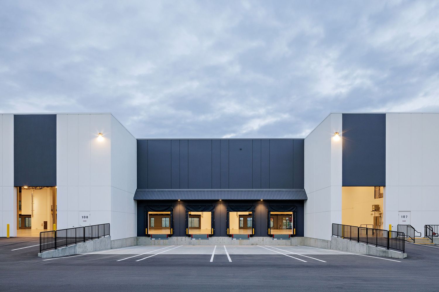 Minimalist commercial building exterior with navy blue and white facade featuring loading bays and ramps at dusk.