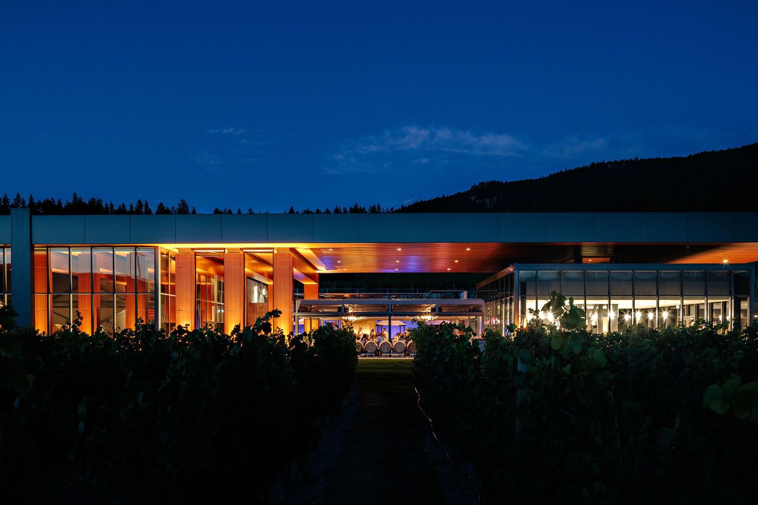 A modern commercial building illuminated at dusk with warm lighting and a deep blue sky overhead.