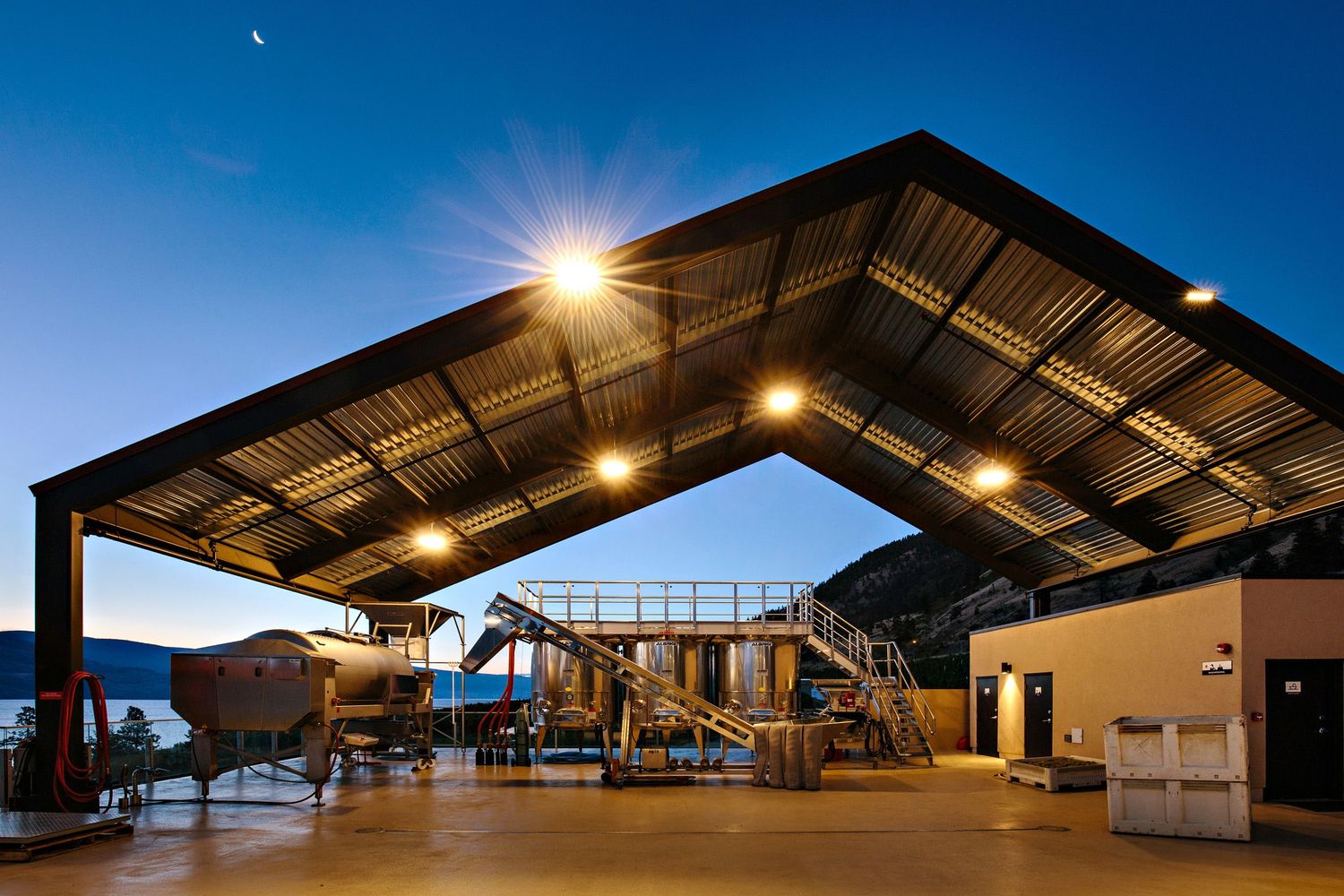 Solar-powered covered playground structure illuminated at dusk with moon visible in blue sky.