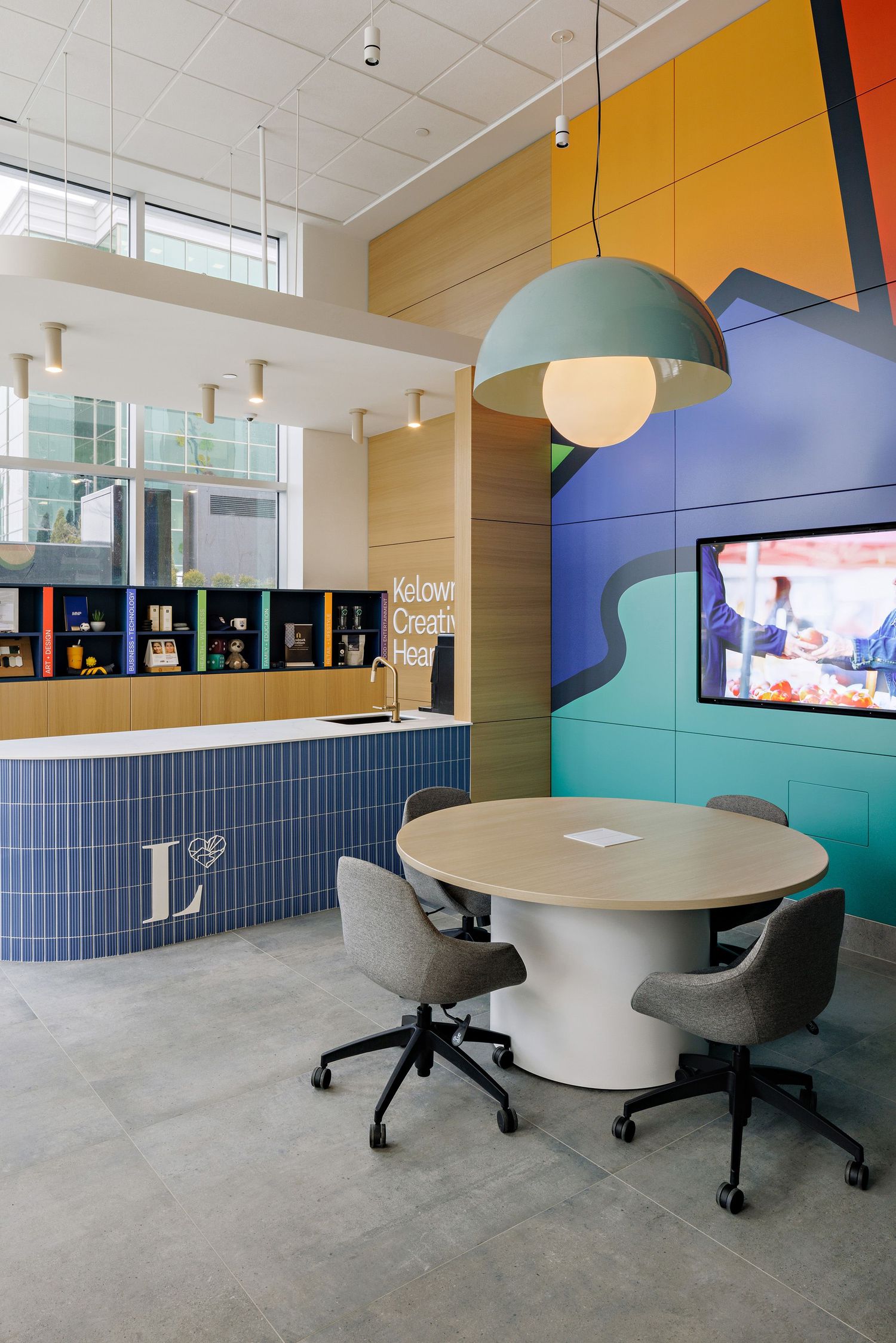 Modern office lounge area with colorful walls, blue tile counter, dome pendant light and round meeting table with chairs.