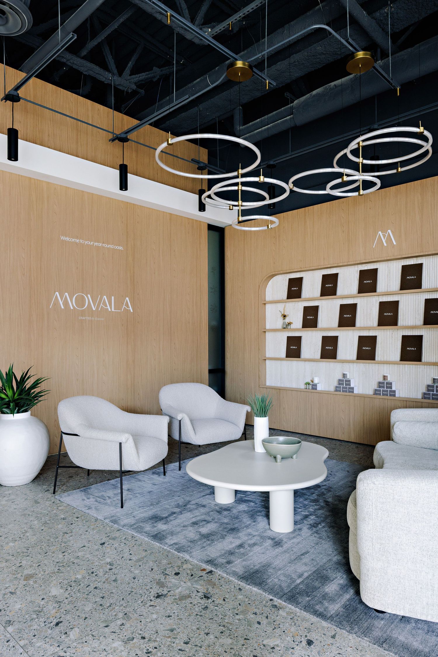 Modern spa lobby interior with circular LED ceiling lights, white lounge chairs and wood panel walls featuring the Movaia brand.