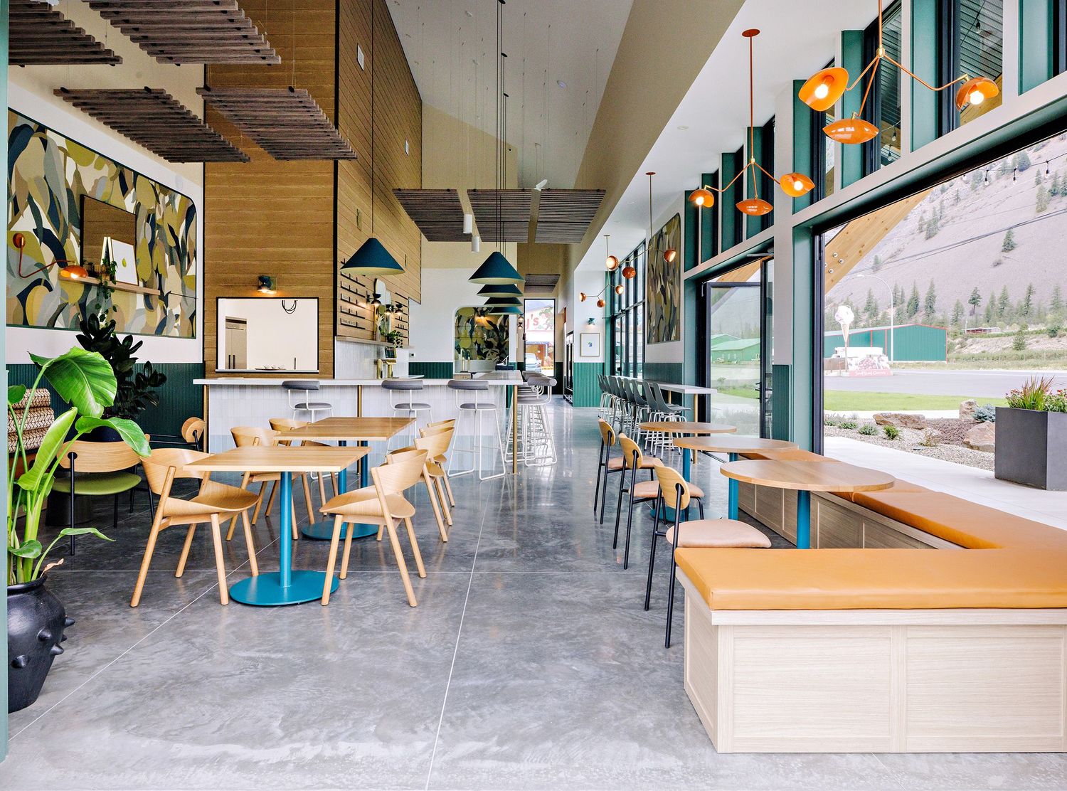 Bright restaurant interior with wooden tables, grey floors and colorful wall murals in a contemporary design.
