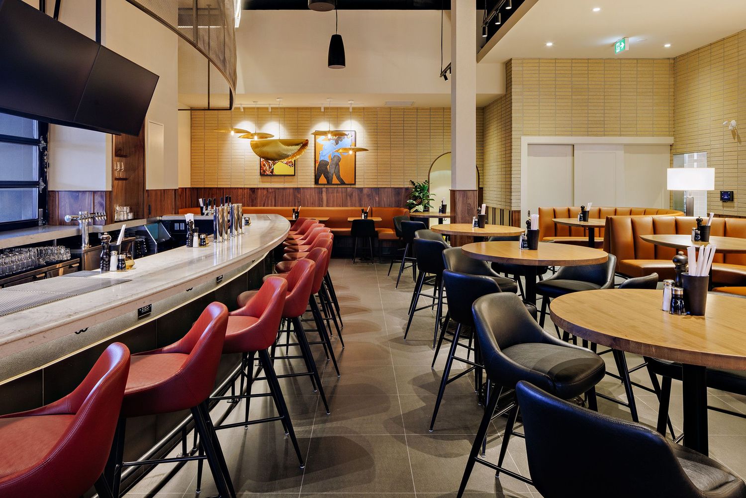 Modern restaurant interior with curved bar seating featuring red bar stools and wood tables in warm lighting.