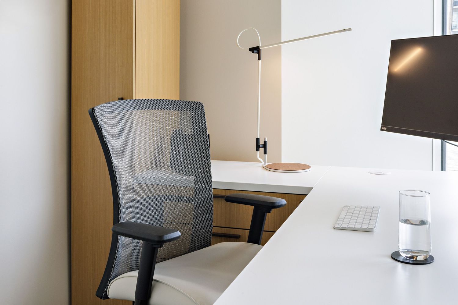 Minimalist office workspace with ergonomic mesh chair, white desk, and mounted monitor.
