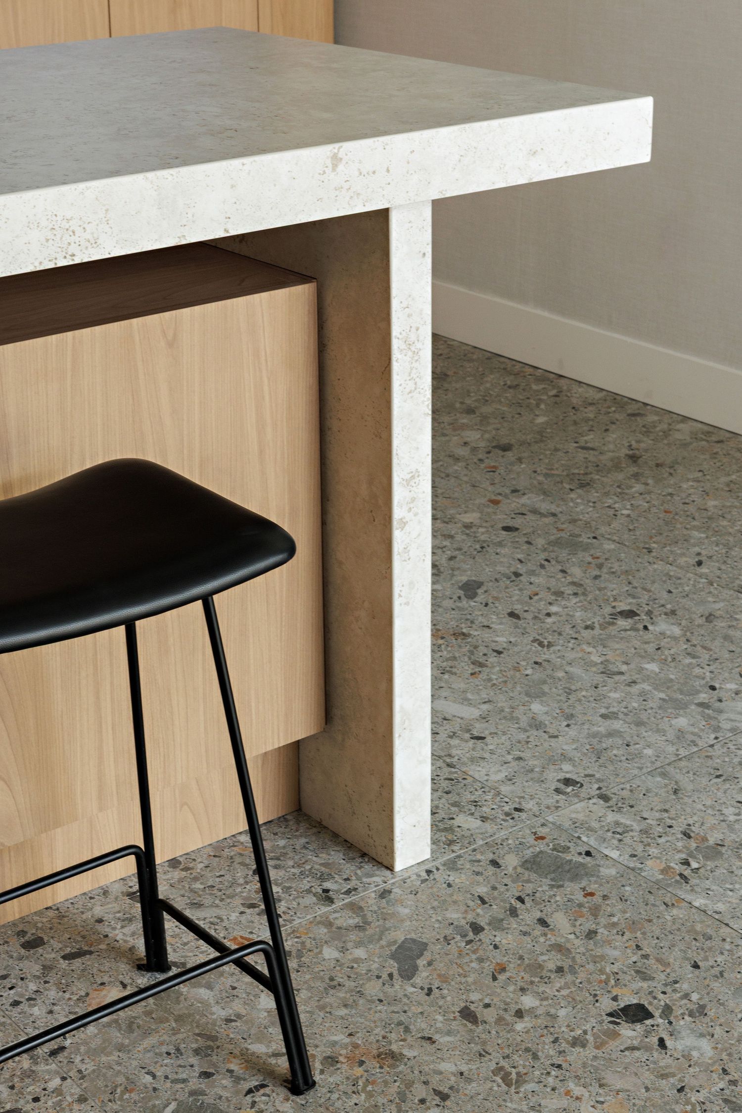 A minimalist corner showing a black metal bar stool against light wood cabinetry with a concrete counter and floor.