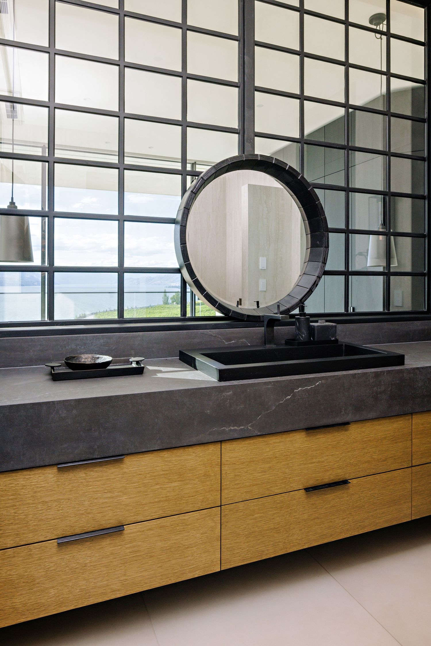 Modern bathroom vanity with wood cabinets and black countertop featuring round mirrors in a contemporary space.